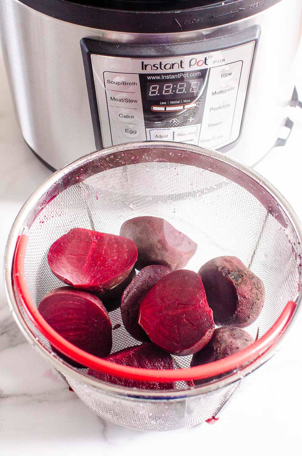 Sliced cooked beets in a steamer basket next to instant pot.