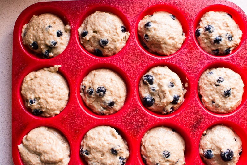 Blueberry muffin batter distributed in red silicone muffin tin.