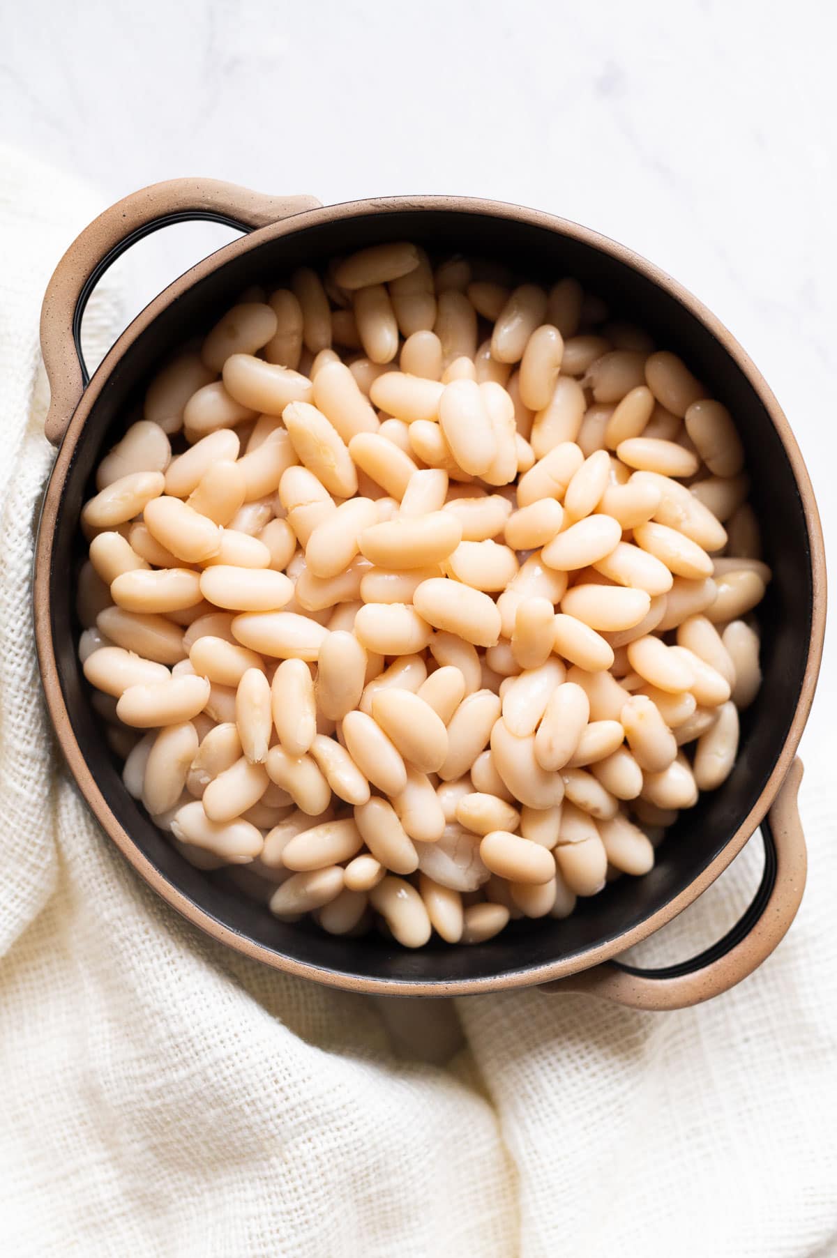 Cooked cannellini beans in a black bowl. Linen towel around it.